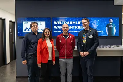 Bild mit 4 Personen vor den Empfangsbildschirmen