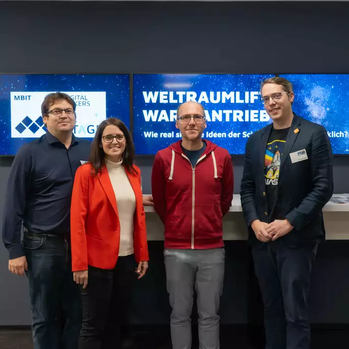 Bild mit 4 Personen vor den Empfangsbildschirmen